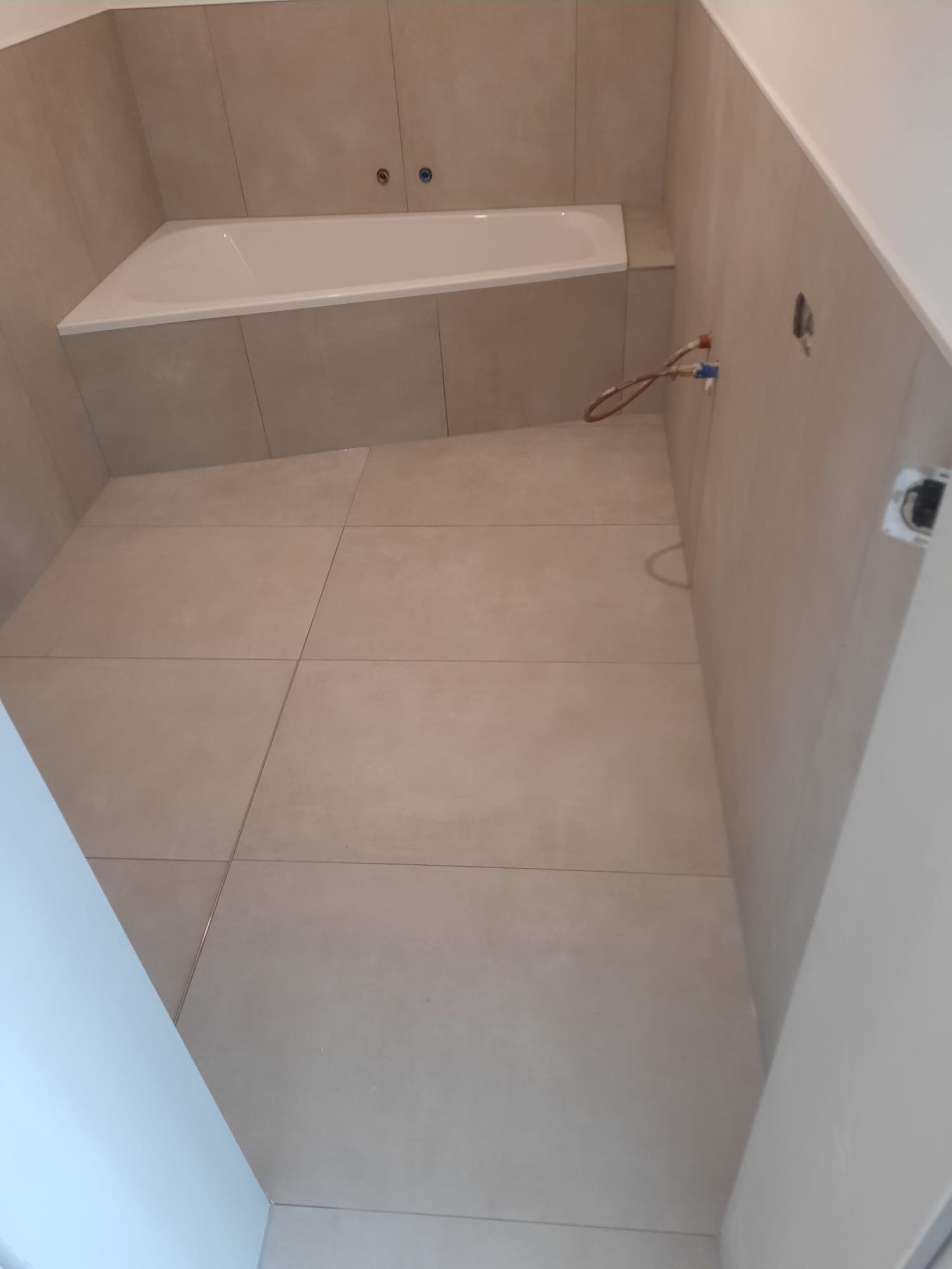 Professionell verlegte Eckbadewanne mit modernen Großformatfliesen in Schieferoptik
